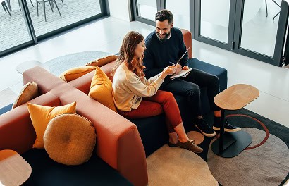 Deux collègues souriants discutent d'un projet dans un cadre moderne et convivial, illustrant un échange professionnel efficace et agréable au sein d'un cabinet de conseil.