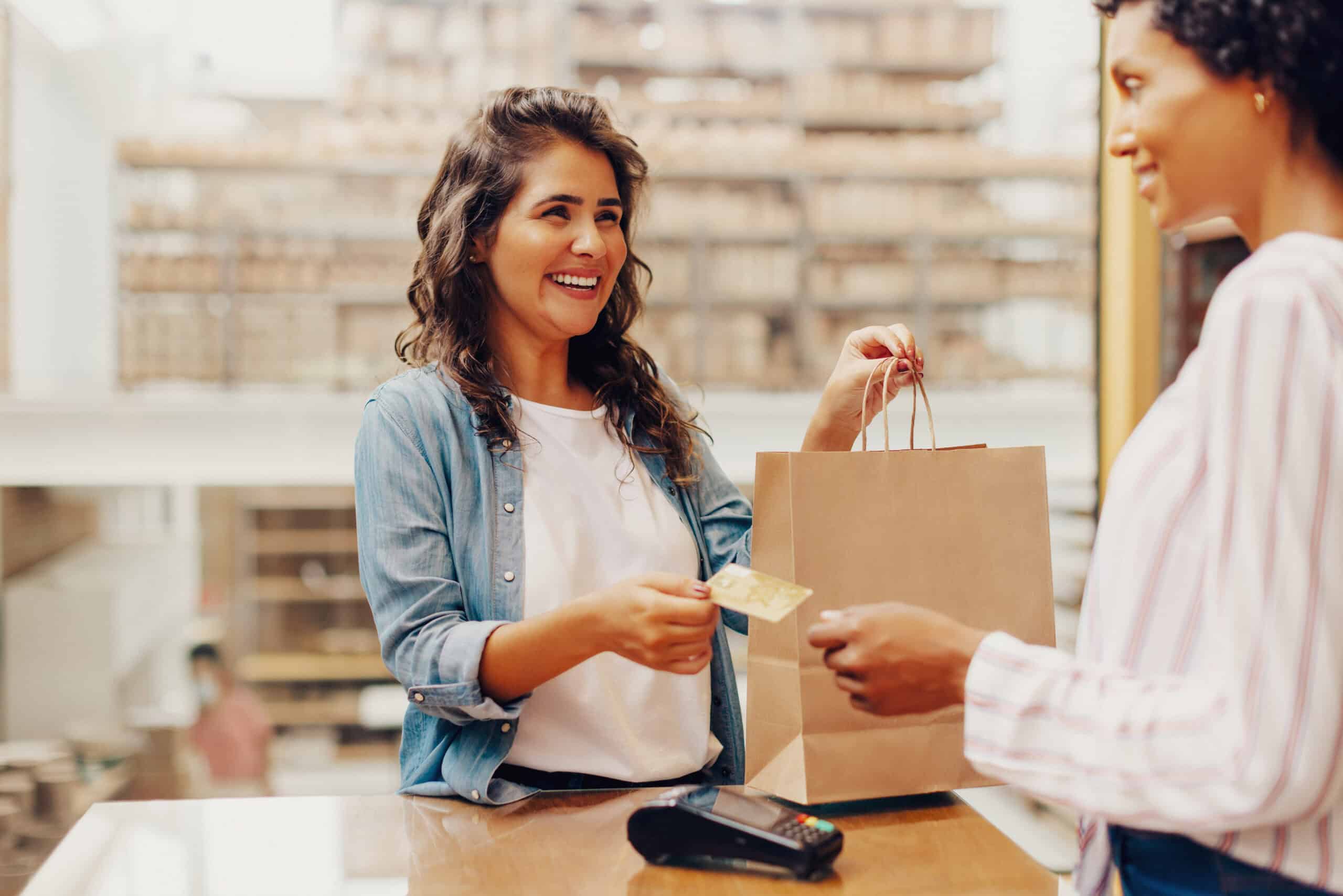 Une cliente prend un sac dans la main et remet sa carte bancaire avec son autre main à une venseuse dans un magasin.